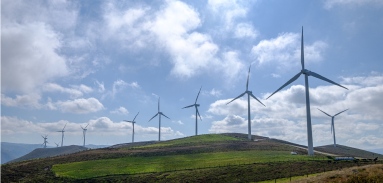 Wind turbines on a hill with blue skies and clouds. Power & Energy industry uses digital twin tech.